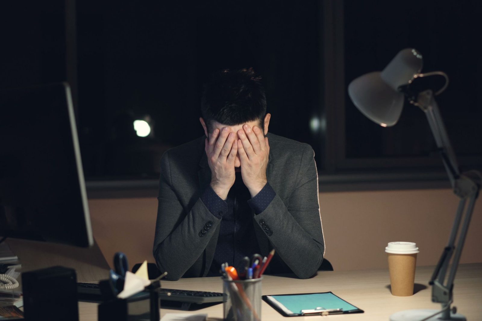 Someone sitting at a desk late at night with their head in their hands